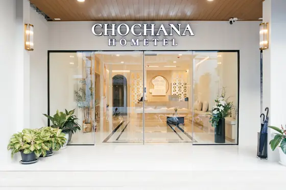 Hotel entrance with glass doors, brass wall lamps, plants and white lilies