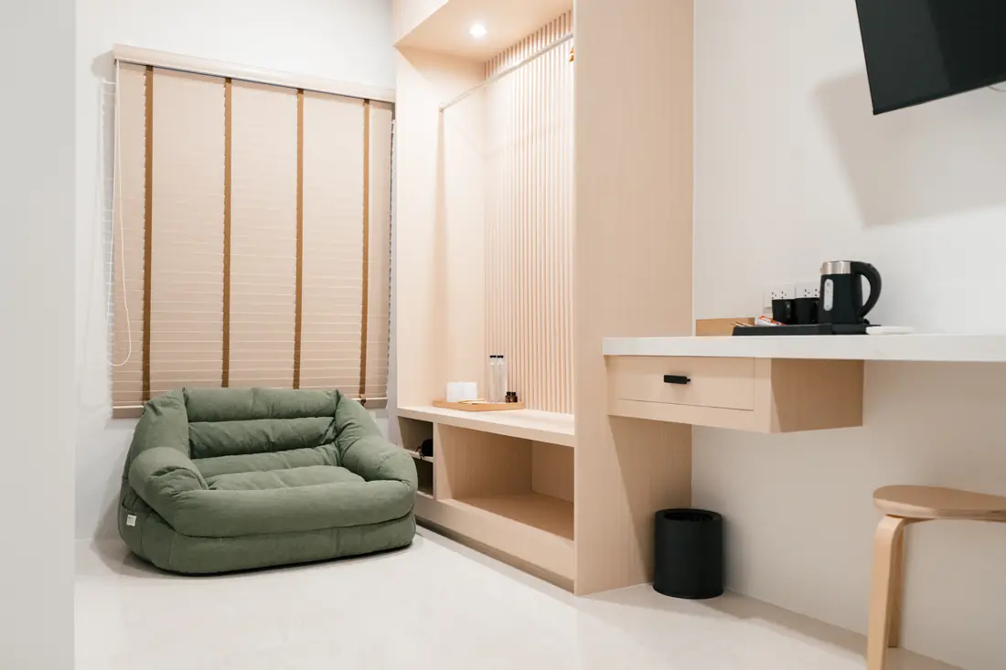 Deluxe room corner with a green sofa under a window with wooden blinds, an open wardrobe and a desk