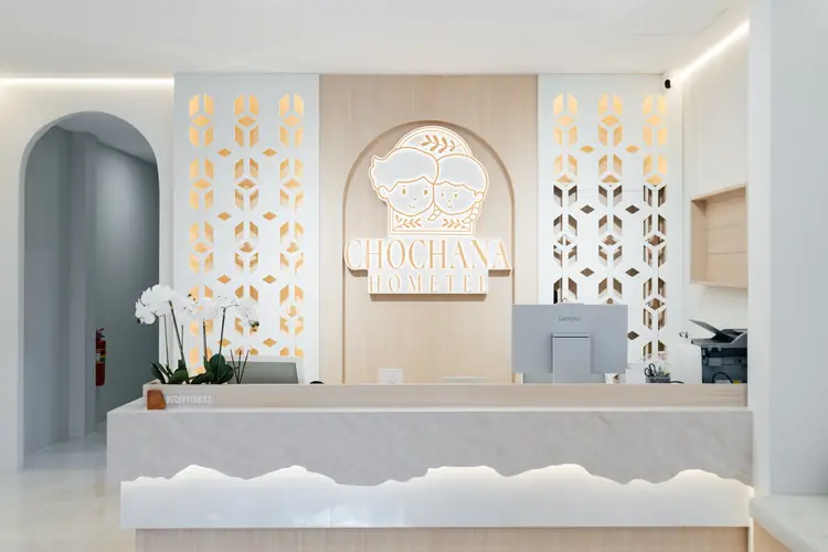 The front desk at Chochana Hometel with white orchids and the lit logo wall